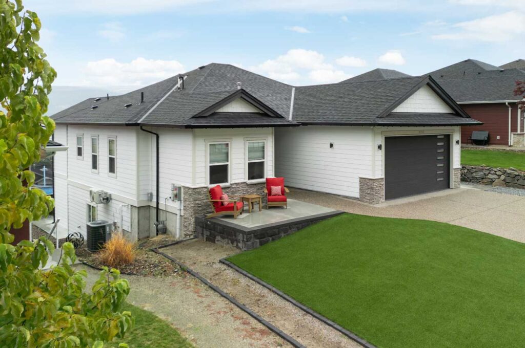 Exterior house painting on a modern West Kelowna home with white siding, black trim, and stone accent base – complete curb appeal transformation